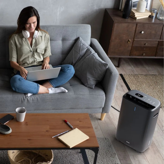 Woman using a laptop on a sofa with the Ionmax Venta ION615 Desiccant Dehumidifier in the foreground